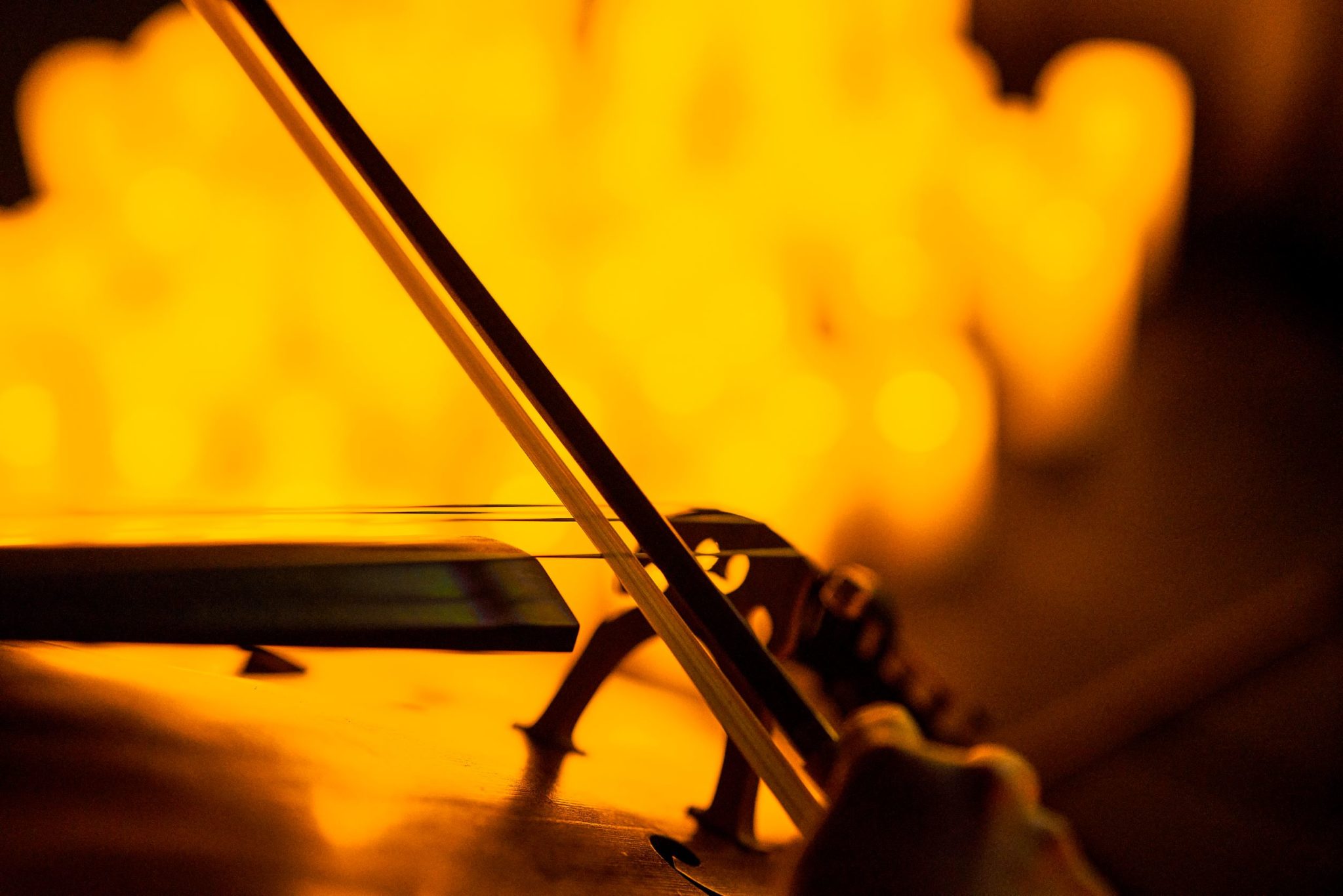 A close-up of a bow playing a string instrument with the blurry images of candles in the background.