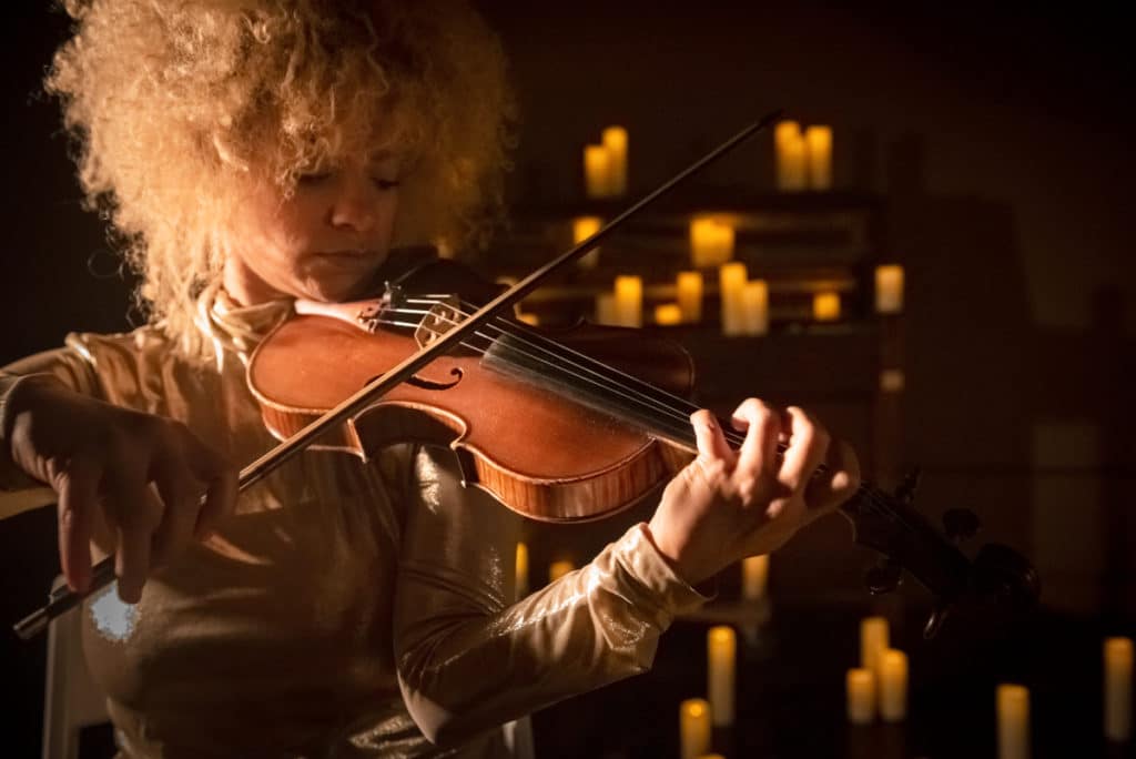 A close-up of a woman playing the violin surrounded by candles 